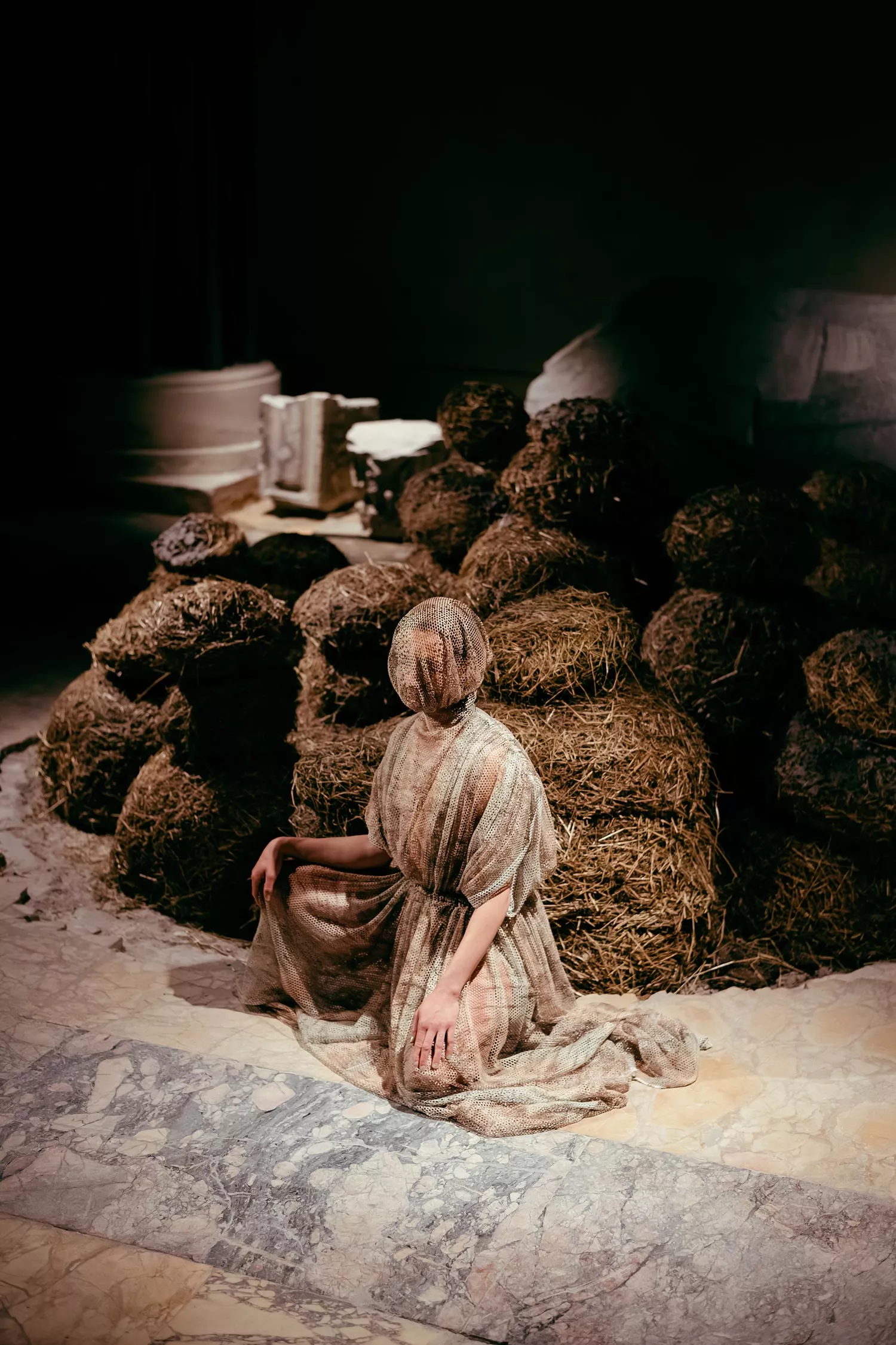 Gaia Fugazza - Gaia Fugazza, 2024, Farewell to Known Skies. Gaia Fugazza, dressed in netting covering her face before a hay installation by Augustas Serapinas
